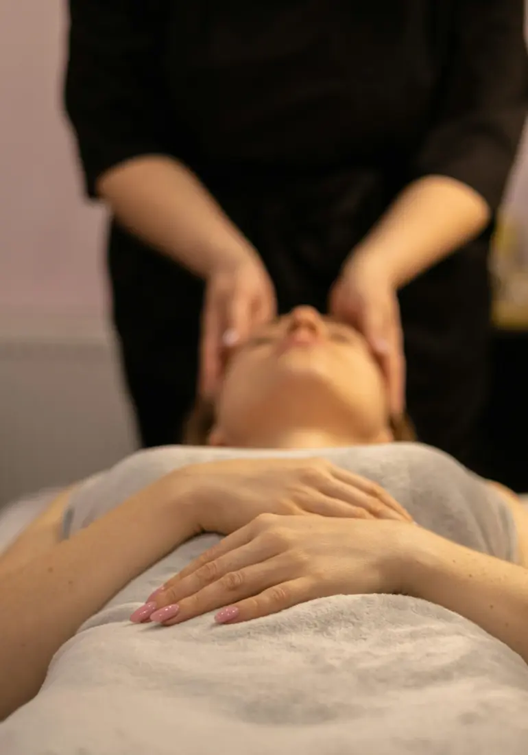 Esthetician's hands cradling a client's face on a treatment bed