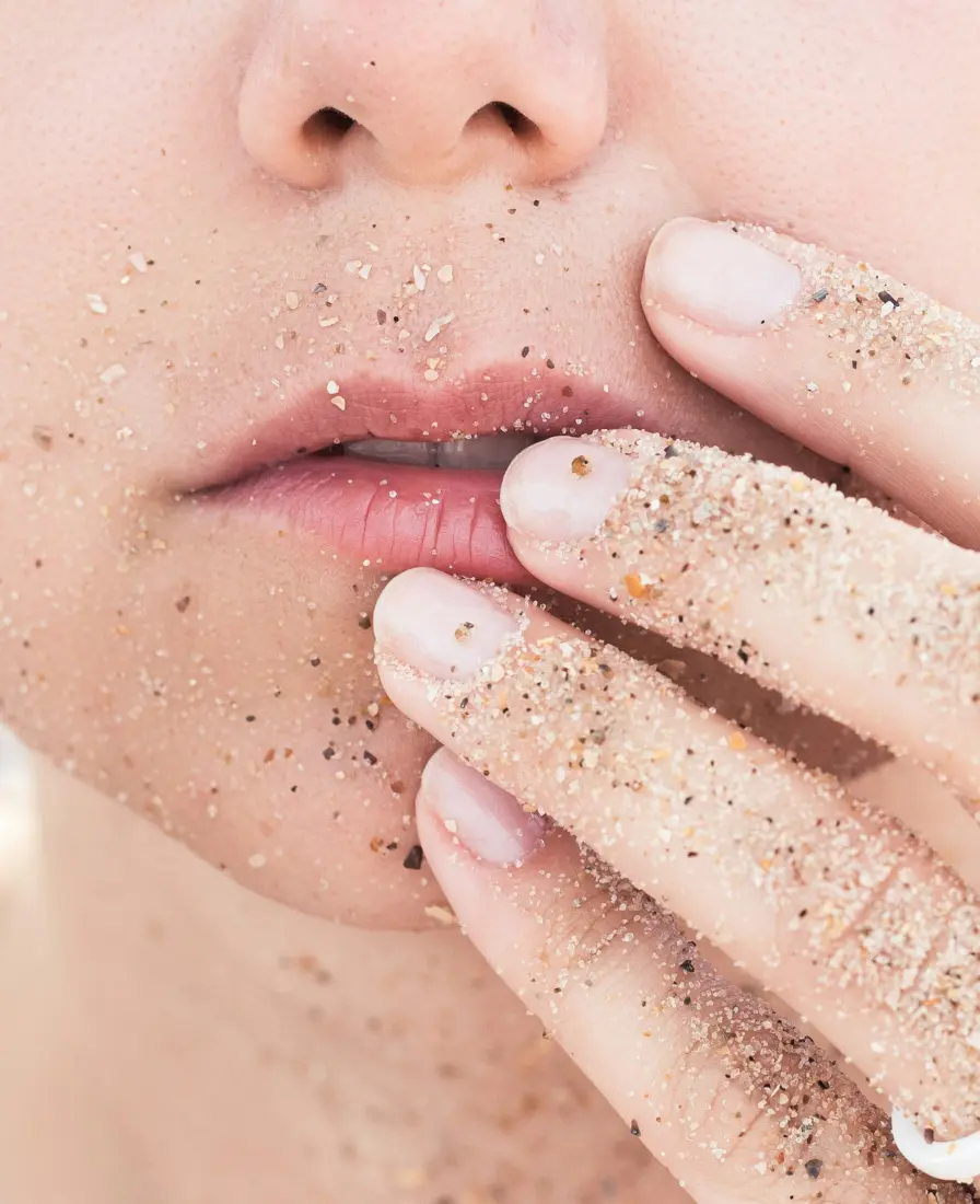 Fingers with grainy scrub touching a woman's lips and chin