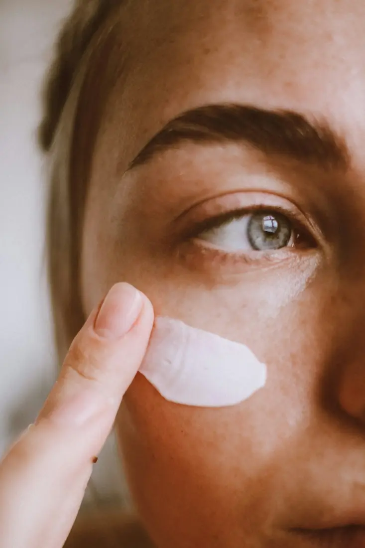 Fingertip smoothing moisturizer onto a woman's freckled cheek
