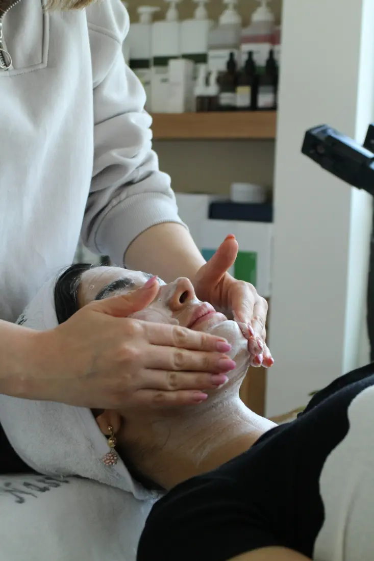 Esthetician's hands cleansing a client's face during a facial