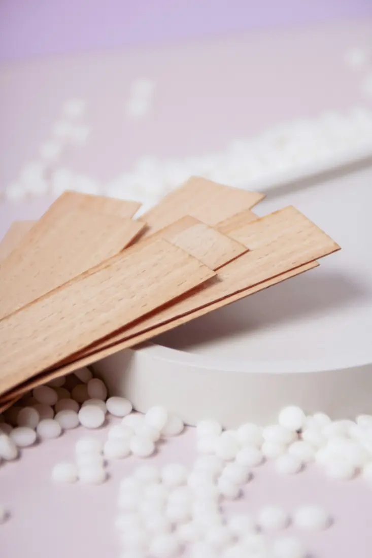 Wooden waxing strips and white wax beads on a pink surface