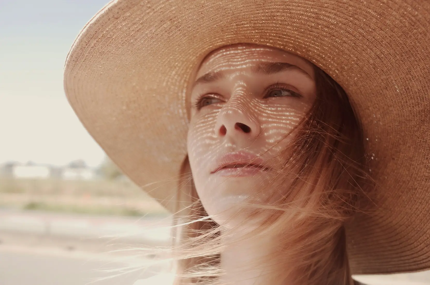 Woman in a wide straw hat with dappled sunlight on her face
