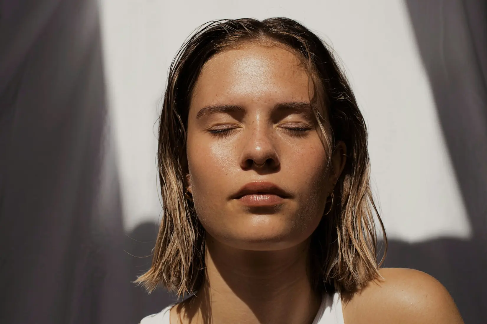 Woman with damp hair and eyes closed in bright sunlight