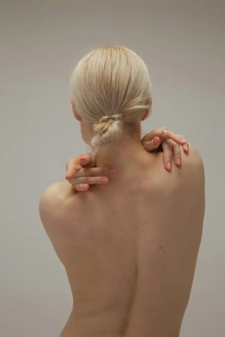 Blonde woman seen from behind with hands on her bare shoulders