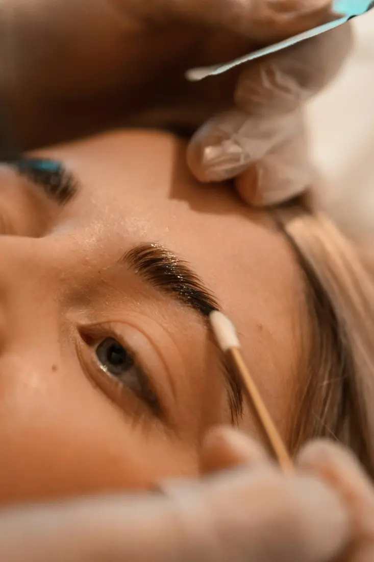 Applicator brushing tint onto a woman's eyebrow, seen close up