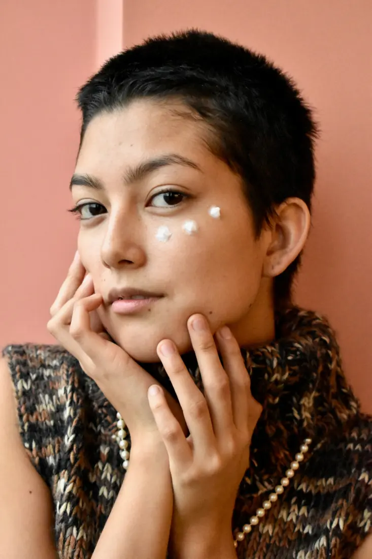 Woman in a knit sweater with dots of cream on her cheek