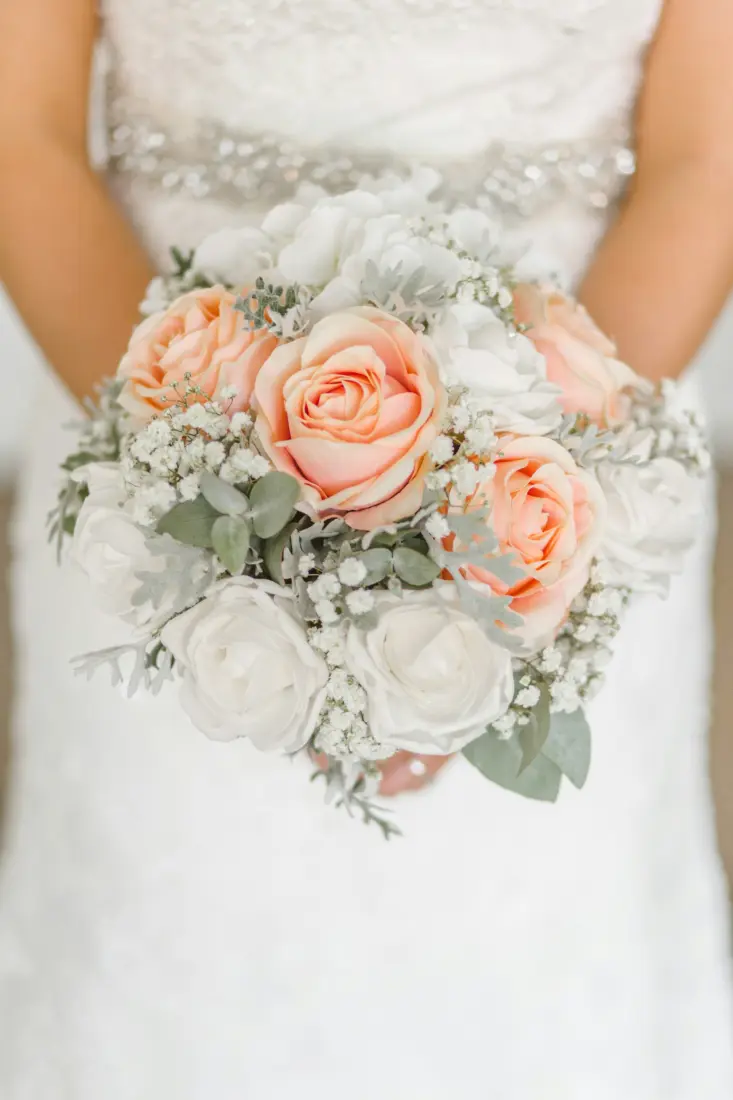 Bride in a white dress holding a peach and white rose bouquet