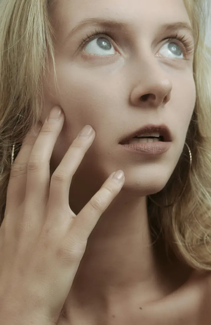 Woman's fingertips resting on her cheek beside her lips