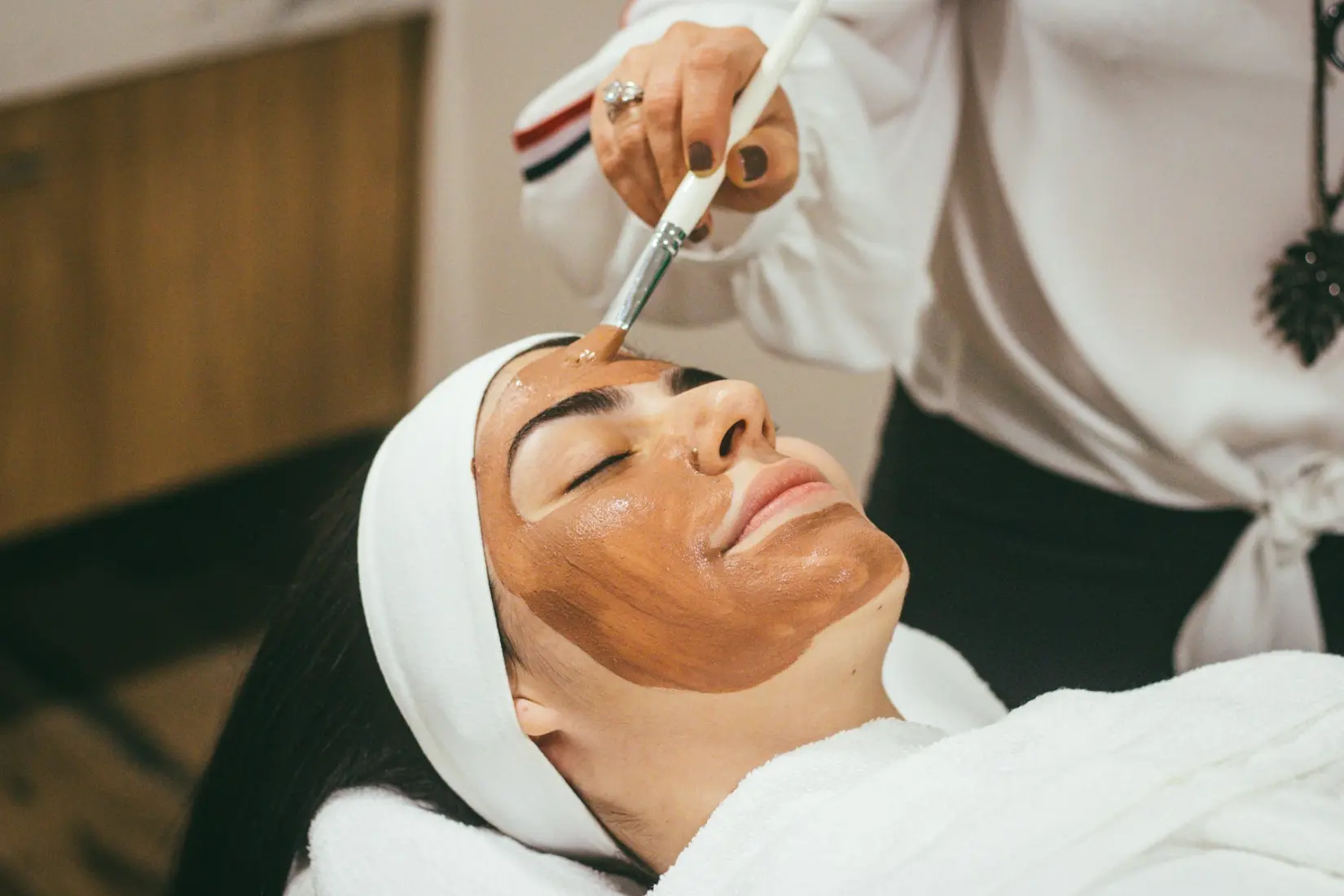 Esthetician brushing a clay mask onto a client's forehead